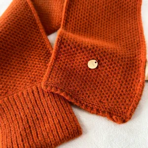 Oranger Strickschal Detail mit Waffelmuster und Metallschild, gemütliches Winter Accessoire.