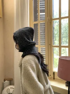 Detailed side view of a dark knitted balaclava hood worn in a warm indoor room.
