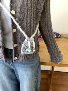 Primer plano del minibolso de punto cruzado con correa mullida y abalorios decorativos.