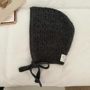 Dark grey knitted balaclava hat detail, hollow-out texture, tie-up ear-protecting hood.