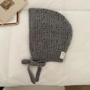 Grey knitted balaclava bonnet detail view, hollow pattern and side tie strings for cozy winter wear.