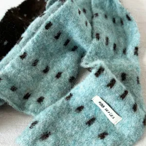 Close-up shot of fluffy knit winter scarf featuring dark spots pattern and brand tag detail.