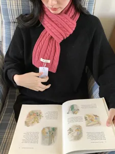 Detail view of a cozy pink cable knit wool scarf worn with black sweater and a book prop.