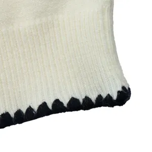 Close-up detail view of knit cardigan sweater, white ribbed fabric with black contrast trim.