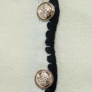 Close-up detail of women's knit cardigan featuring elegant gold buttons and contrast black trim.