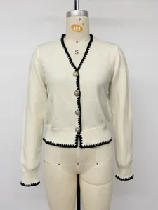 Detailed view of white knit cardigan with black trim and gold buttons on mannequin display.