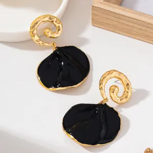 Gros plan de boucles d'oreilles noires et dorées avec motif spirale martelée et pétale.