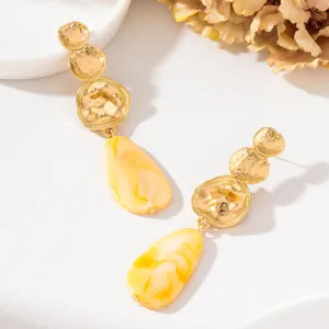 Gros plan détaillé de disques en or martelé élégants avec des boucles d'oreilles en résine jaune.