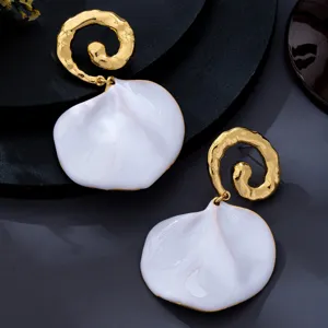 Vue en gros plan de boucles d'oreilles spirales texturées dorées et pétales blancs, détail chic.