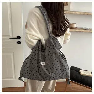 Vista detallada del bolso tote de lona gris oscuro con estrellas llevado al hombro.