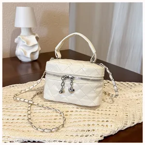 Close up detail of white quilted mini vanity bag with chain strap and cute heart charm pendant.