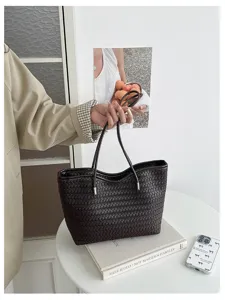 Dettaglio borsa tote intrecciata marrone scuro con texture in pelle e manici.