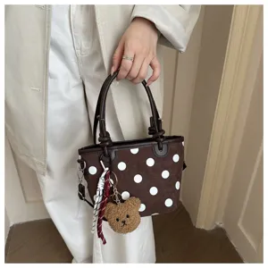 Dettaglio borsa a secchiello marrone a pois chic, con grazioso ciondolo orsetto di peluche.