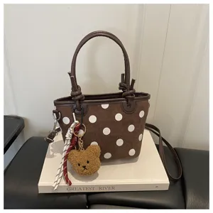 Dettaglio borsa a secchiello a pois marrone, con simpatico portachiavi orsetto e tracolla.