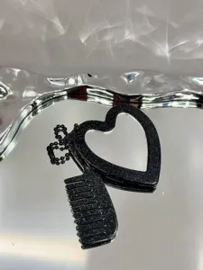 Detailopname van een zwarte glitter hart zakspiegel en kam sleutelhanger op dienblad.