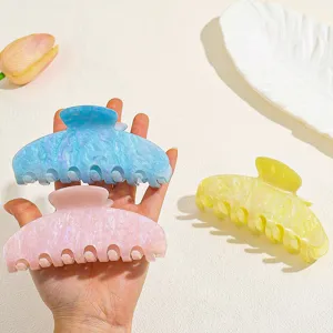 Detail shot of glossy pearl-effect hair claw clips in pastel blue, pink, and yellow.