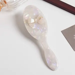 Pearlescent acetate hair brush with cute bow detail, smooth and portable daily styling tool.