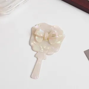 Acetate bow handheld makeup mirror detail view, elegant pearly finish cosmetic vanity tool.