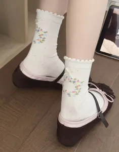 Detailaufnahme weißer Socken mit Rüschenrand, süßer Blumenstickerei und 3D-Schleife hinten.