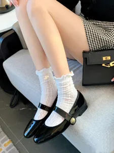 Close-up detail shot of white lace ruffle socks and black patent leather Mary Jane shoes.
