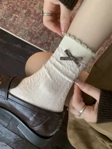 Detail van retro witte middelhoge sokken voor dames met volants, kabelbreisel en strik.
