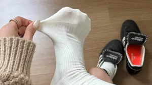 Detailed view of white ribbed socks showing elastic stretch texture with sneakers nearby.