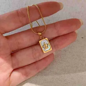 Gros plan de collier pendentif carte de tarot en acier inoxydable doré, perle blanche.