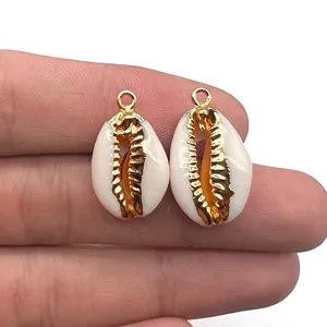 Gros plan de pendentifs en coquillage cauris naturel avec anneaux dorés pour la fabrication de bijoux.