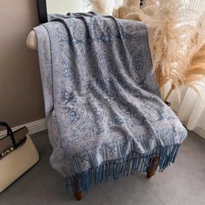 Elegante scialle blu con motivo Paisley e frange drappeggiato su sedia in interno.