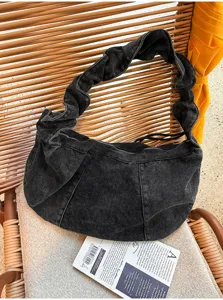 Close-up of black washed denim hobo shoulder bag with unique pleated strap design detail.