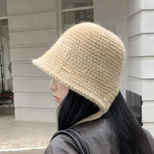 Beige knit bucket hat detail showcasing soft texture, warm ear flap design and side metal tag.