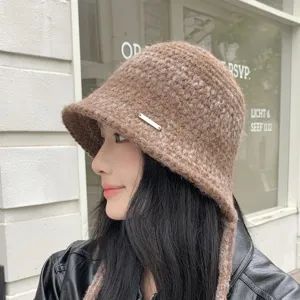 Detailed shot of brown knitted bucket hat with side metal badge and chin straps.
