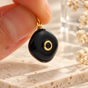 Close-up detail van zwarte onregelmatige natuurstenen hanger met gouden hardware accenten.
