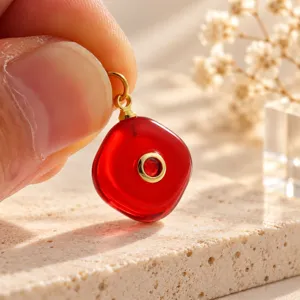 Close-up van rode snoephanger met gouden oogje en centrale steen voor DIY sieraden maken.