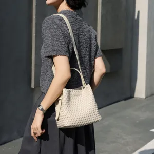 Détail en gros plan du sac seau en cuir tressé beige porté élégamment en extérieur.