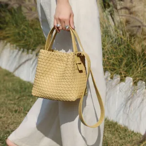 Chic sac seau tressé en cuir jaune clair, doté de poignées supérieures et d'une bandoulière réglable.