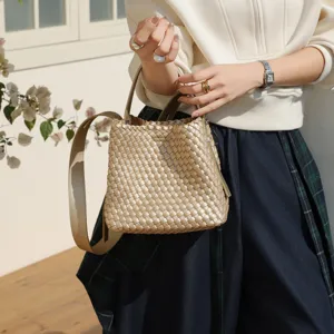 Détail du sac seau tressé en or métallisé avec poignée supérieure et bandoulière chic.