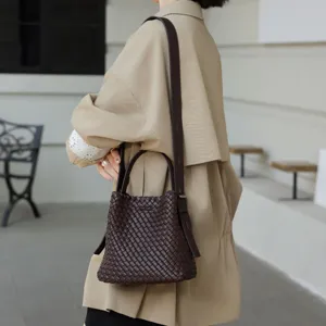 Détail de sac seau en cuir tressé marron foncé, sac bandoulière et porté épaule élégant.