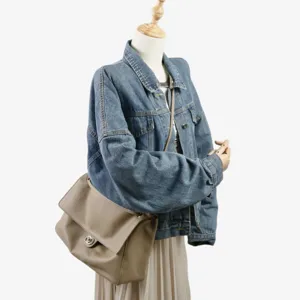 Grand sac a epaule en cuir souple avec veste en jean et jupe plisee sur mannequin de vitrine.