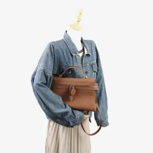 Sac bandoulière en cuir marron en détail, montrant une texture fine, une fermeture et des poignées.