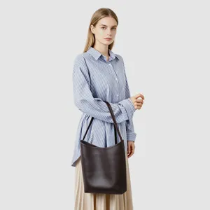 Modella che indossa un'elegante borsa a secchiello in pelle marrone scuro con dettagli.