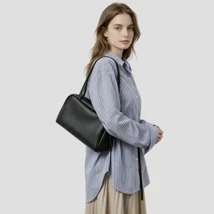 Vue détaillée du sac porté épaule bowling en cuir noir, porté par un mannequin en tenue.