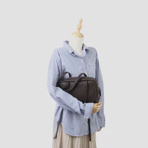 Vue détaillée du sac boston en cuir marron foncé présenté sur un mannequin avec chemise rayée.