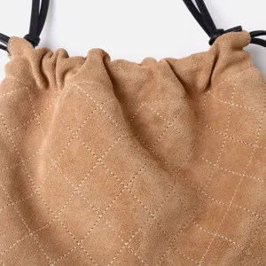 Détail de sac bourse matelassé en suédine chameau avec coutures losanges et cordon noir.