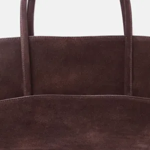 Gros plan détaillant les poignées et la texture du sac cabas en cuir suédé marron foncé.