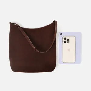 Détail de sac à épaule en daim marron montrant la comparaison de taille avec le smartphone.