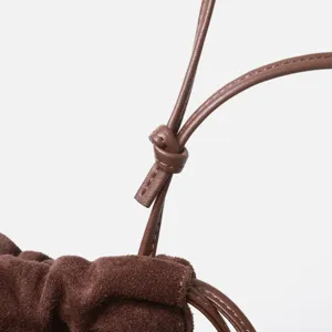 Gros-plan du sac cordon en daim marron, texture de cuir nubuck souple et nœud élégant.