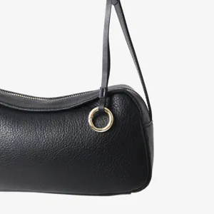 Gros plan sur les détails d'un sac à main en cuir noir avec texture souple et anneau doré.