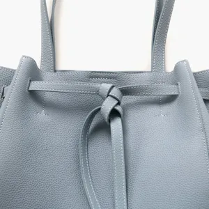 Vue détaillée du sac cabas en cuir gris-bleu avec design de sangle à nœud, texture premium.