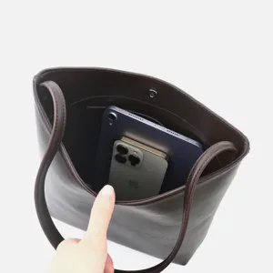 Dettaglio della capacità interna della borsa secchiello in vera pelle con telefono e tablet.